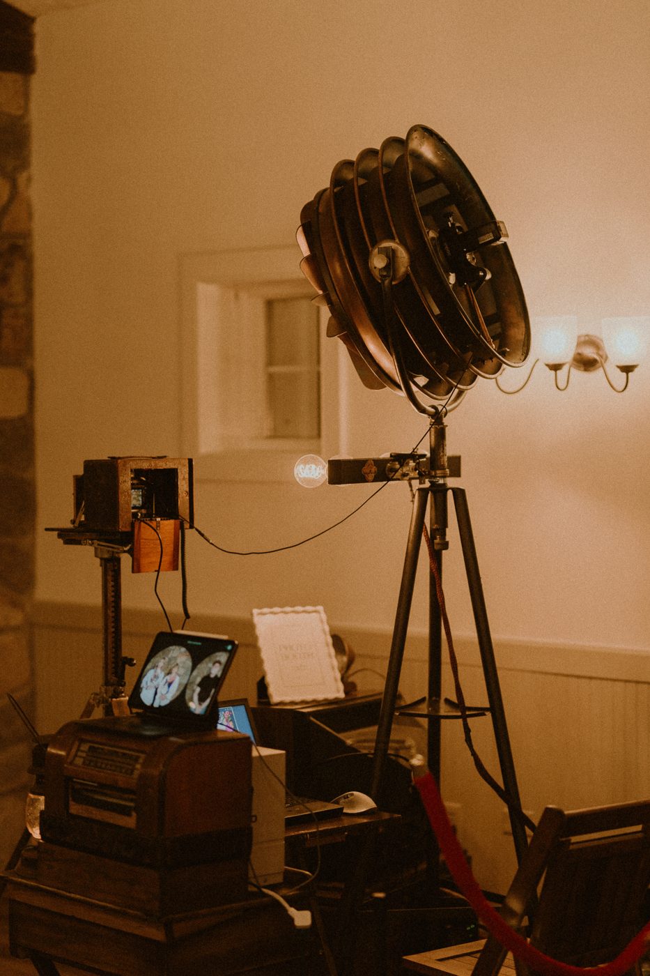 The Copper&Velvet booth from behind — the restored copper lamp fixture and bellows camera, warmly lit at a reception.