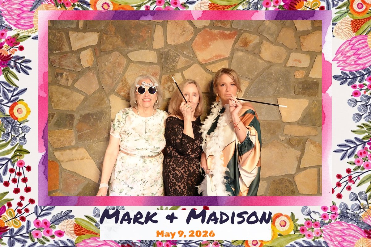 Three guests posing with cigarette-holder props in front of the booth's stone backdrop, printed with the Mark & Madison photo template.